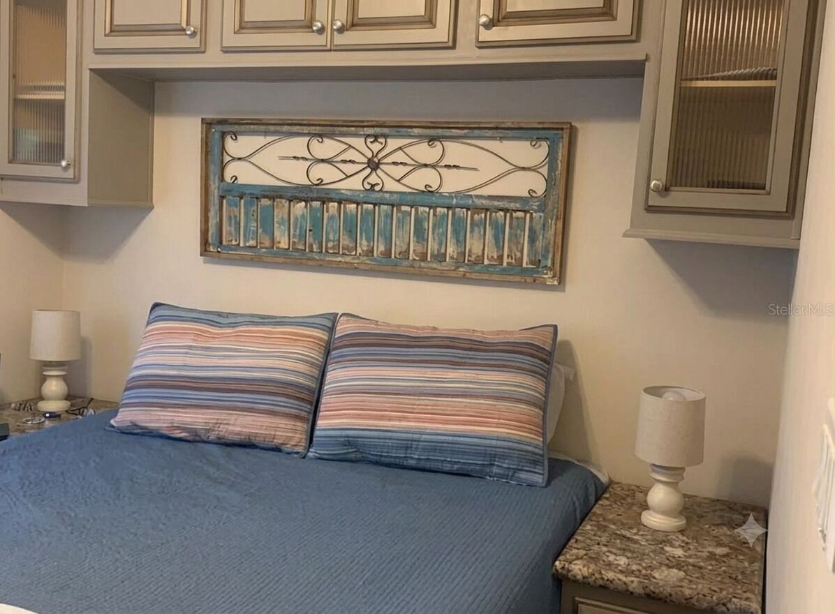 Ein Schlafzimmer mit einem Bett, zwei Nachttischlampen, einem dekorativen Metallkunstwerk über dem Bett und hellen Schränken.