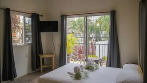 Una habitación de hotel con cama, televisor montado en la pared, una mesita y un balcón con una silla.