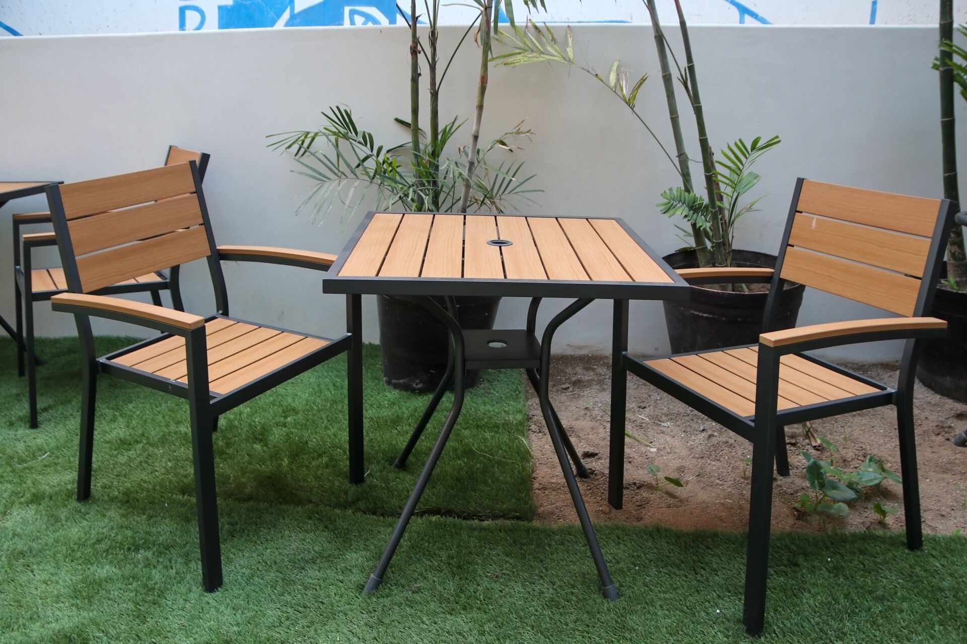 A patio with a table and four chairs, surrounded by potted plants and a wall.