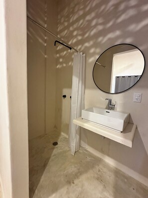 Un baño con ducha, lavabo, espejo y un interruptor de luz.