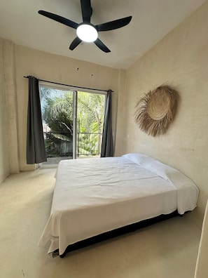 A bedroom with a bed, a ceiling fan, a window with curtains, and a wall-mounted decorative item. - Patio Canarias Suites Pet-Friendly (Chacala)