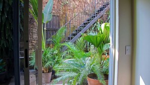 Un espacio exterior estrecho con plantas en macetas, una escalera de metal y una valla de madera.
