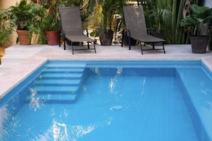 A swimming pool with two lounge chairs and potted plants around.