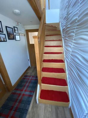 A wooden staircase with red carpeted steps leading to a room with a white curtain.