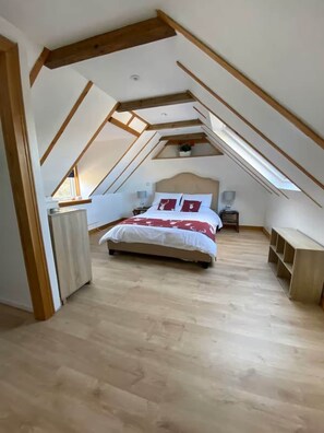 A bedroom with a sloped ceiling, a bed with red bedding, a bedside table, a lamp, and a small shelf.