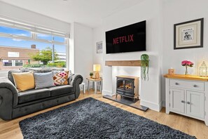 Ein Wohnzimmer mit einer Couch, einem Kamin, einem darüber montierten Fernseher und einem Fenster mit Blick auf Gebäude.