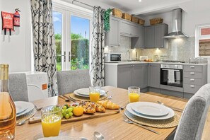 A modern kitchen with grey cabinets, a stainless steel range hood, and a dining area with a wooden table set for breakfast. - Spacious Home with Garden for Groups & Families (Greater Manchester)