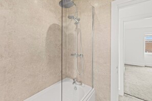 A modern bathroom with a glass-enclosed shower, a standalone bathtub, and a visible door leading to another room. - Spacious Home with Garden for Groups & Families (Greater Manchester)