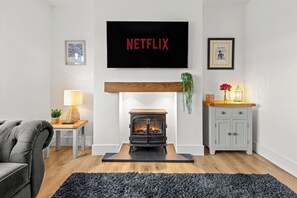 A living room with a fireplace, a television mounted above it, a sofa, a small table with a lamp, and a cabinet. - Spacious Home with Garden for Groups & Families (Greater Manchester)
