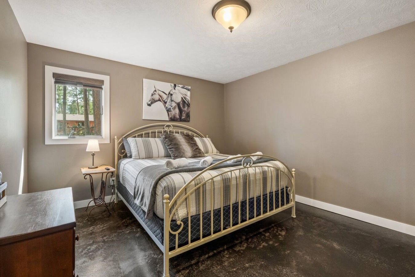 A bedroom with a bed, a nightstand, a lamp, a window with a view of trees, and a ceiling light fixture.