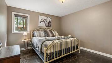 A bedroom with a bed, a nightstand, a lamp, a window with a view of trees, and a ceiling light fixture.