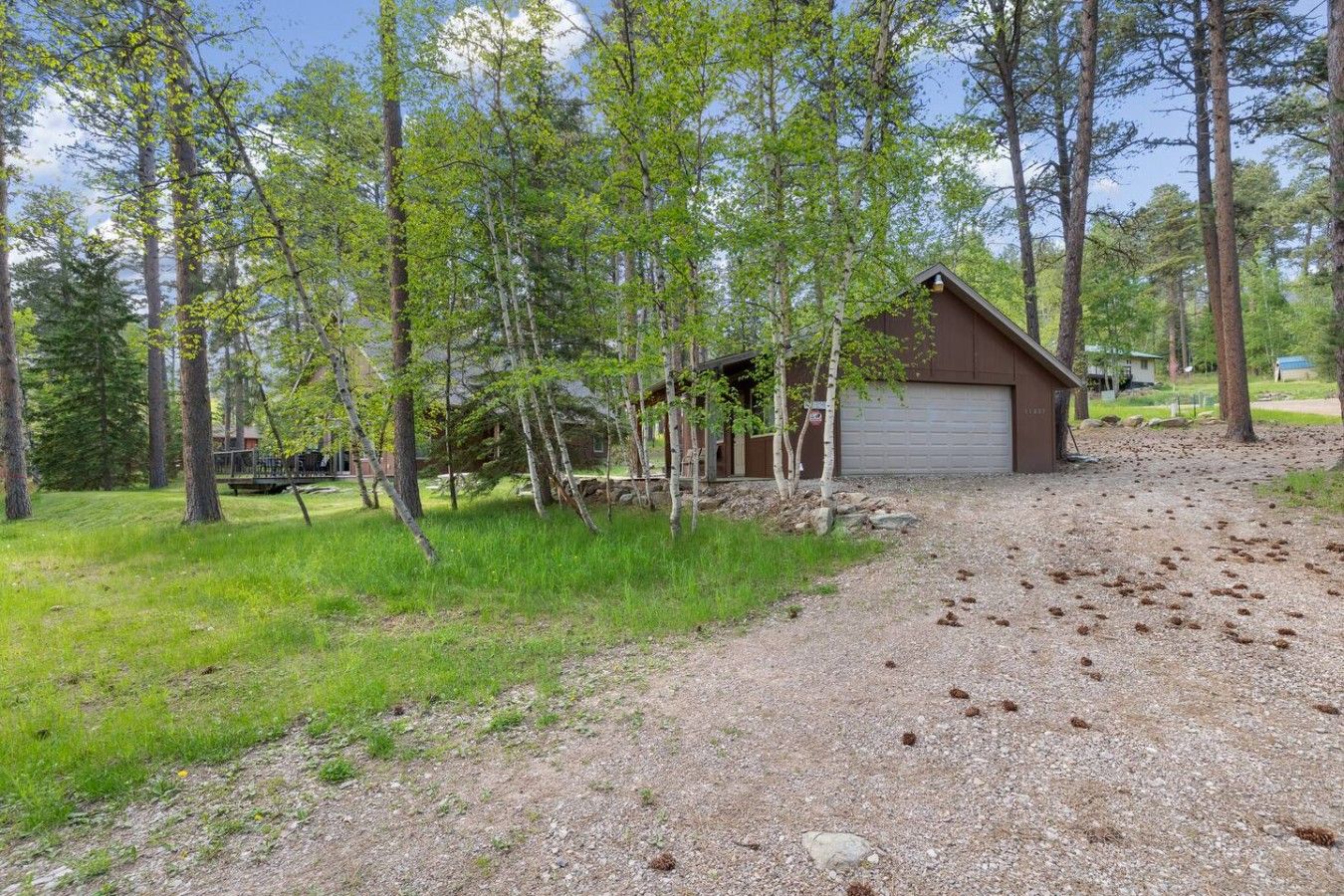 A gravel driveway leading to a wooden cabin with a garage, surrounded by trees and a grassy area.