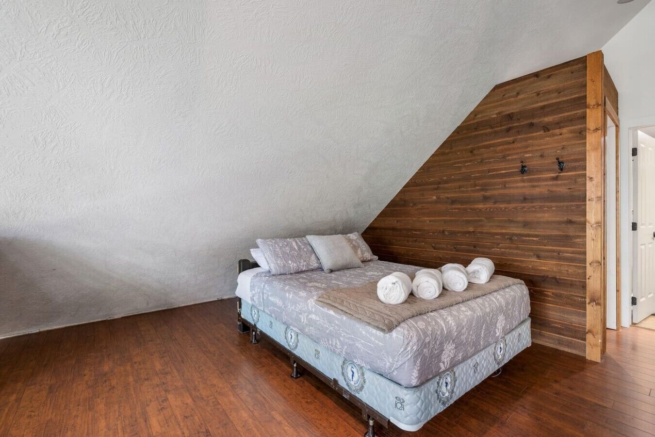 A bedroom with a sloped ceiling, a bed with a patterned mattress, pillows, and rolled towels on the floor.