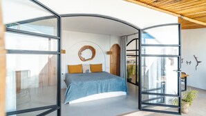 A modern bedroom with a bed, a circular wooden wall decoration, and a view of the outside. - 5 Villas | 5 Private Pools | Tamarindo | 14 Guests (Tamarindo)