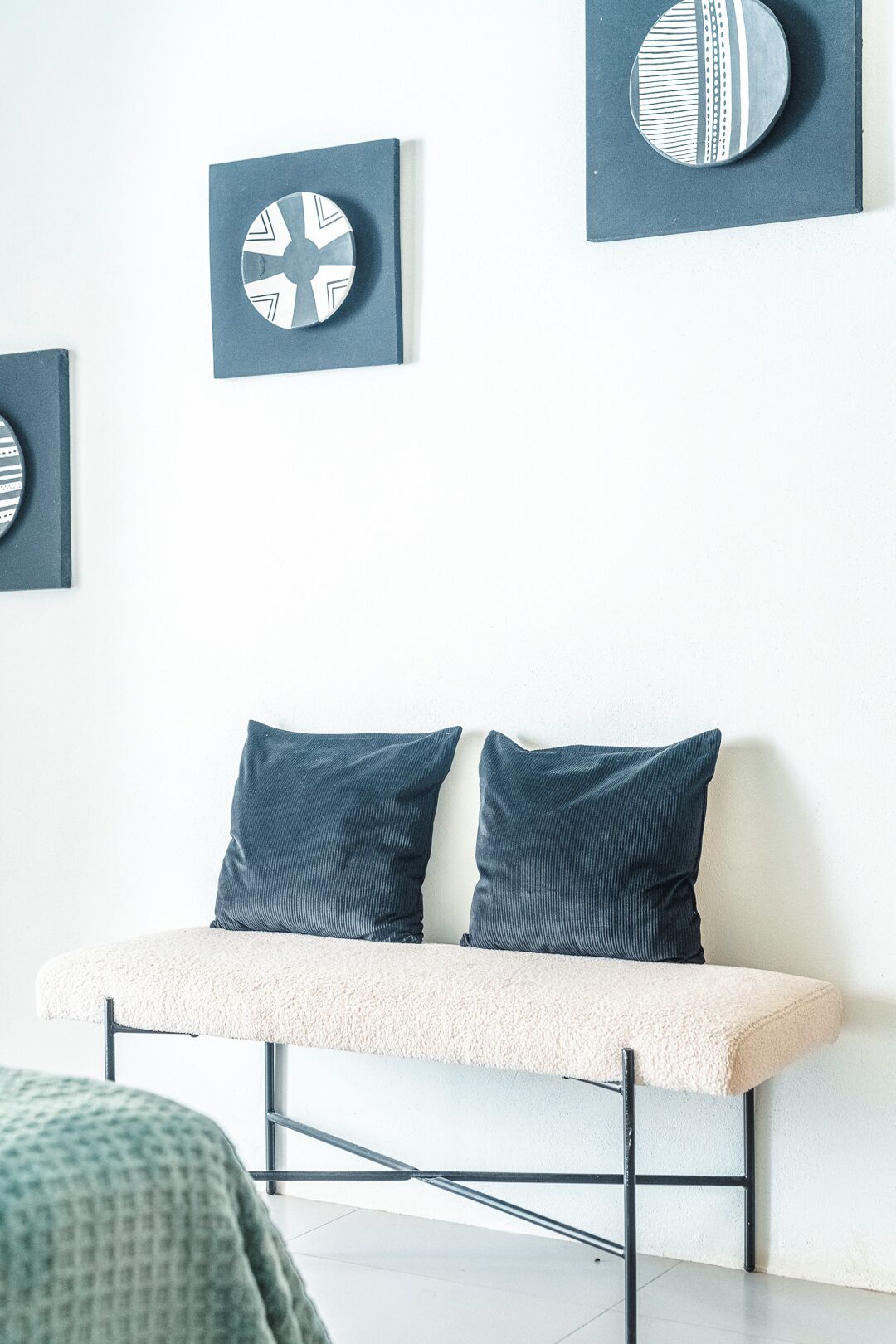 Habitació moderna amb una boscadeira i dos coixins, una paret blanca amb textura i tres elements decoratius circulars a la paret.
