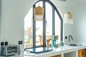 Eine Küche mit einem großen Fenster, einer Kaffeemaschine, einem Toaster und hängenden Makramee-Lampen.