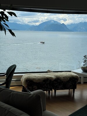 Ein Zimmer mit Blick auf einen See und Berge, ein Sofa, ein kleiner Tisch und eine Zimmerpflanze.