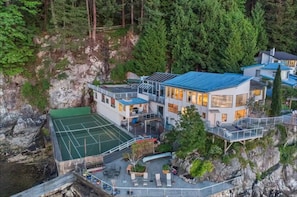 Ein modernes, mehrgeschossiges Gebäude mit Tennisplatz, Außenbereich und Blick auf eine felsige Klippe und einen Wald.