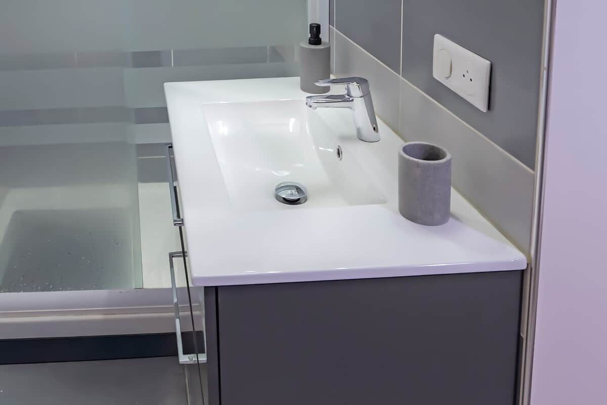 Un baño con un lavabo blanco, una llave de estilo moderno, un dispensador de papel higiénico y una cabina de ducha de vidrio.