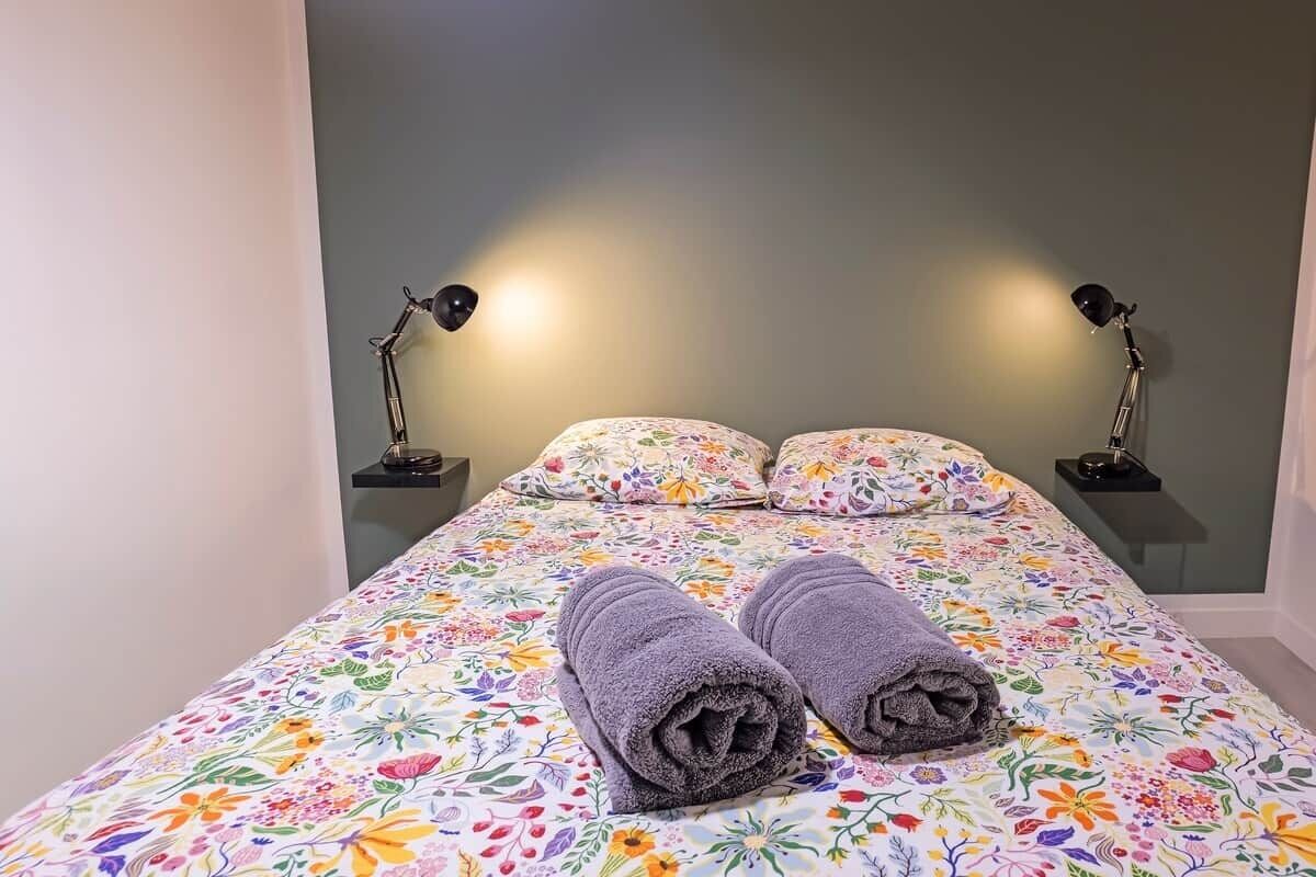 Een bed met bloemenbeddengoed, twee lampen en twee opgerolde handdoeken.