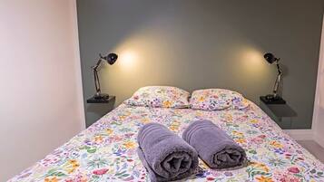 Een bed met bloemenbeddengoed, twee lampen en twee opgerolde handdoeken.