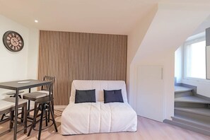 Une chambre moderne comprenant un lit, une table à manger avec des chaises, une horloge murale et une fenêtre.