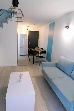 Un salon moderne avec un canapé bleu clair, une table basse blanche et un coin repas comprenant une table et des chaises.