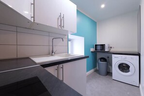 Une cuisine moderne avec des meubles blancs, un plan de travail noir, un évier, un lave-linge et un four à micro-ondes.