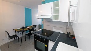 A compact kitchen with a dining table, chairs, and a built-in stove. - GR65 Compostelle stage - Duplex 5 pers -Center Puy (Le Puy)