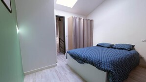 A bedroom with a bed, a skylight, a door leading to a staircase, and a curtain. - GR65 Compostelle stage - Duplex 5 pers -Center Puy (Le Puy)
