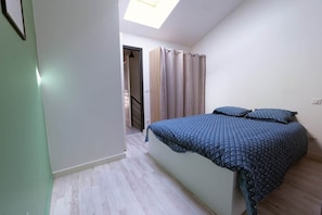 Ein Schlafzimmer mit einem Bett, einem Oberlicht, einer Tür zu einer Treppe und einem Vorhang.