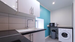 A modern kitchen with white cabinets, a black countertop, a sink, a washing machine, and a microwave. - GR65 Compostelle stage - Duplex 5 pers -Center Puy (Le Puy)
