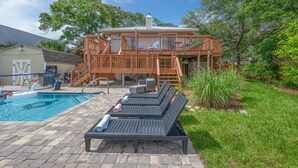 Un espace piscine avec des chaises longues, une terrasse en bois et une maison en arrière-plan.