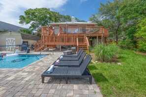 Ein Poolbereich mit Liegestühlen, einer Holzterrasse und einem Haus im Hintergrund.