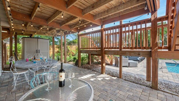 Un espace extérieur aménagé en terrasse, avec une table ronde, des chaises, une bouteille de vin et une piscine en arrière-plan.