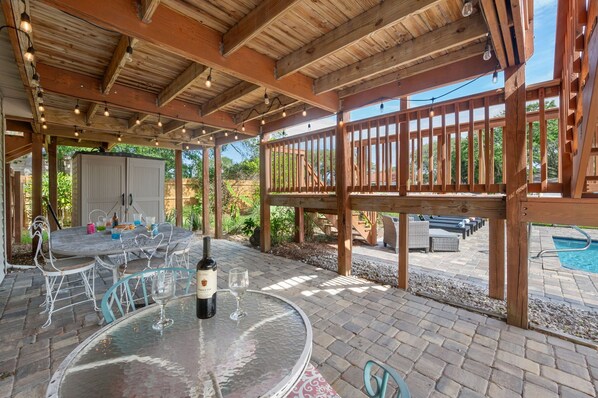 Eine Außenpatio-Terrasse mit einem runden Tisch, Stühlen, einer Weinflasche und einem Pool im Hintergrund.