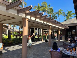An outdoor covered area with a stage, palm trees, and a seating area with tables and chairs. - Quiet Luxury at Kings’ Land – 2BR Villa with Golf & Resort Amenities (Waimea)