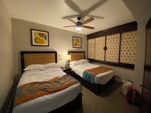 A hotel room with two beds, a ceiling fan, artwork on the walls, and a window with patterned curtains. - Quiet Luxury at Kings’ Land – 2BR Villa with Golf & Resort Amenities (Waimea)