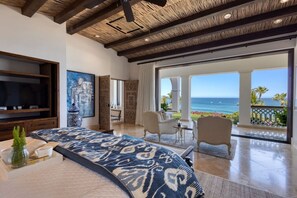Ein geräumiges Schlafzimmer mit einem großen Bett, einem Fernseher, einem Gemälde und Meerblick.