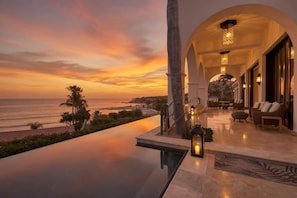 Ein luxuriöses Resort mit Infinity-Pool mit Blick auf den Ozean, einer überdachten Sitzgelegenheit im Freien und einem Sonnenuntergang.