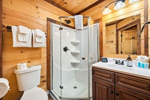 A wooden cabin bathroom with a glass shower enclosure, a toilet, and a vanity with toiletries.