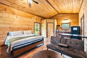 A wooden cabin interior with a bed, sofa, and kitchenette.