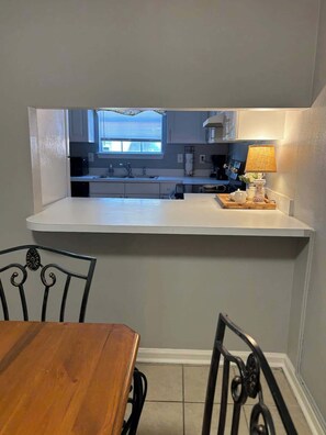 A compact kitchen with a white countertop, a sink, and a window. There is a dining table with chairs in the foreground. - Nice 2 Bedroom/3 Beds/1.5 Bath Apartment - Bryant3 (Bryant)