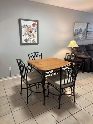 Een eethoek met een houten tafel, vier stoelen, een lamp en een schilderij aan de muur.