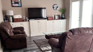 Un salon avec un canapé en cuir marron, une table basse en verre et un téléviseur à écran plat posé sur un meuble blanc.