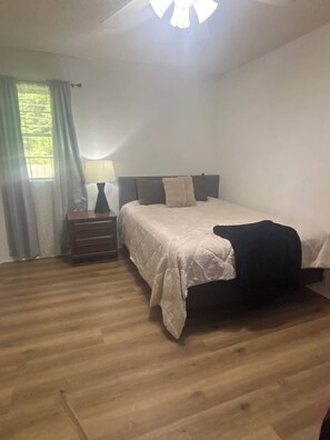 Un dormitorio con cama, mesita de noche, lámpara y ventana con cortinas.