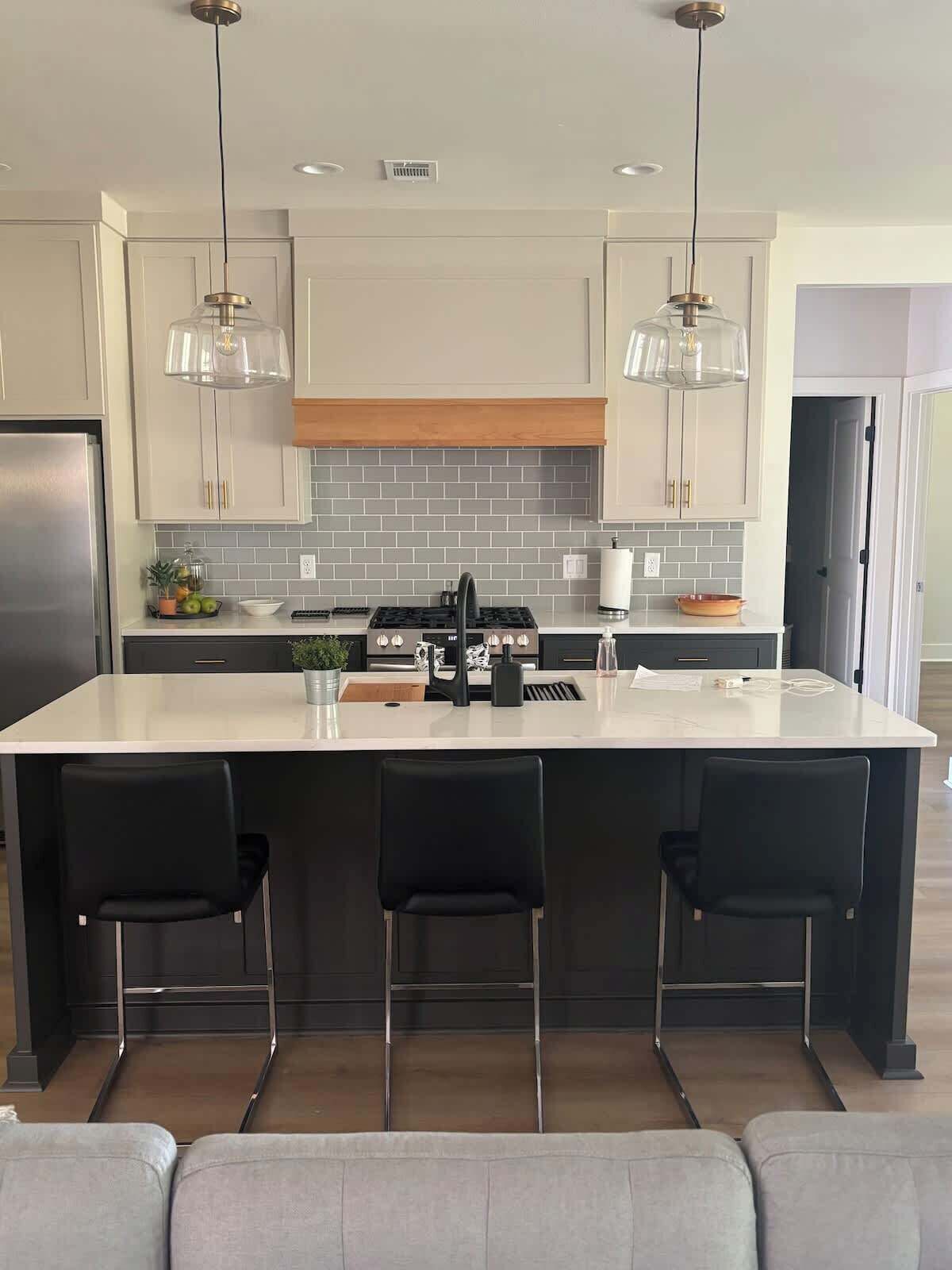A modern kitchen with a central island, black bar stools, and pendant lighting.
