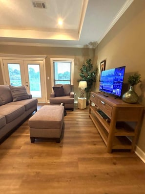 Ein Wohnzimmer mit Sofa, Hocker, Fernseher, Lampe und Couchtisch aus Holz.