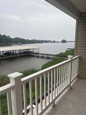 Blick vom Balkon mit Geländer auf ruhiges Gewässer, eine Anlegestelle und Bäume in der Ferne.
