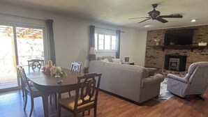 A living room with a dining table, sofa, and chairs, a fireplace, and a ceiling fan. - Large 4 Bedroom Home - Bryant, AR (Bryant)